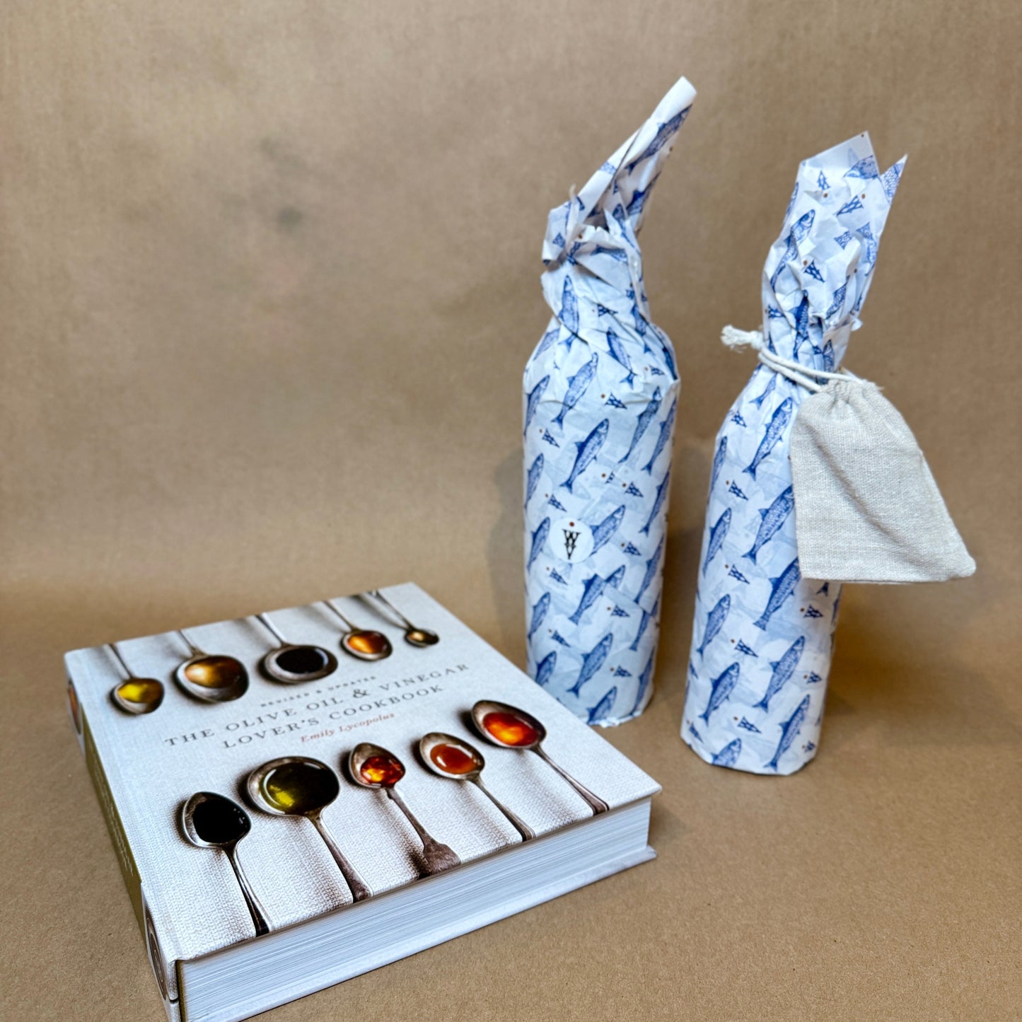 Foodie gift set with two wrapped olive oil bottles and the Olive Oil & Vinegar Lover's Cookbook on a brown background.