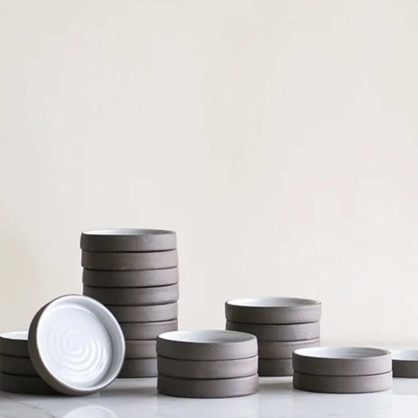 Stacked hand-crafted ceramic dishes in neutral tones, perfect for serving olive oils.