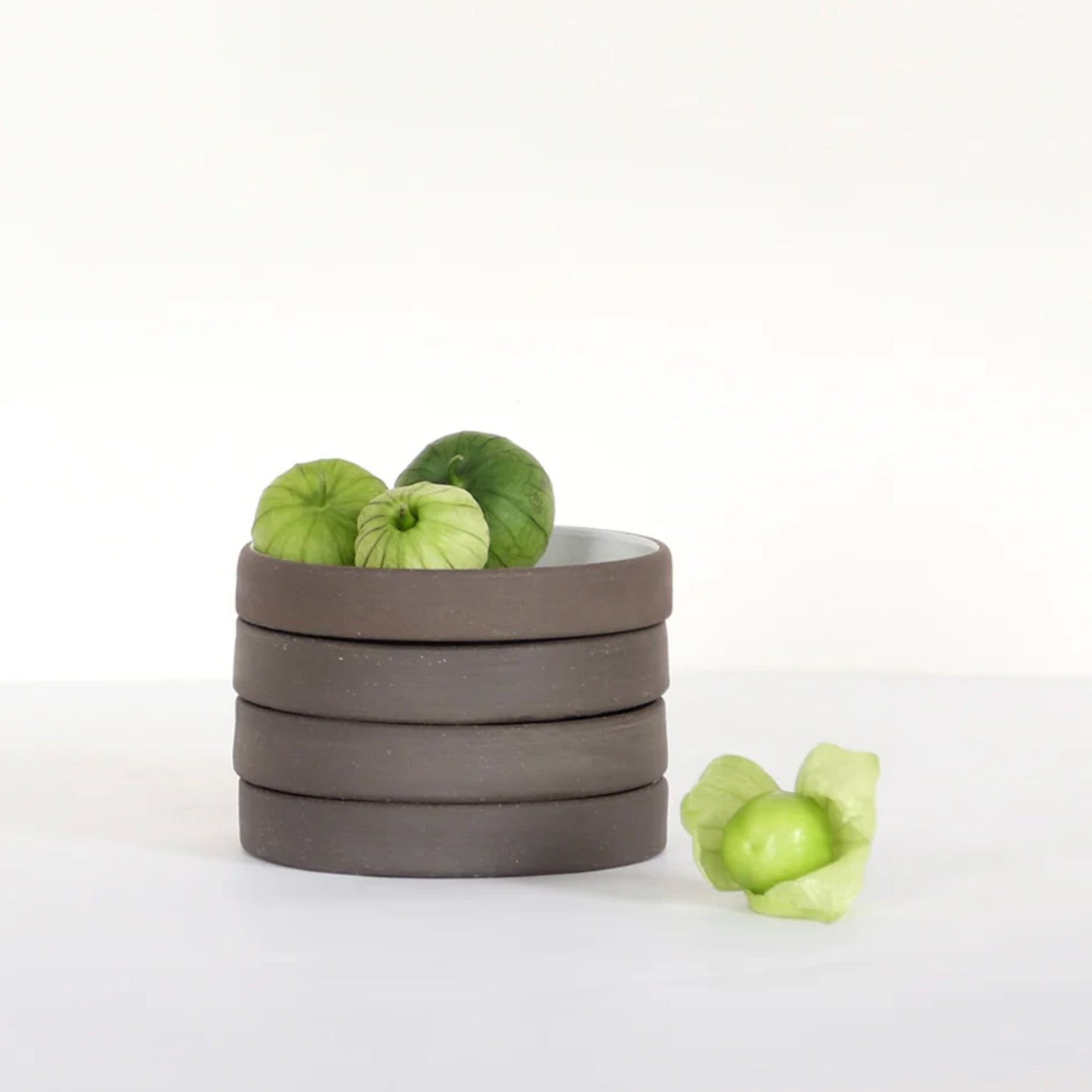Handcrafted ceramic bowl stack with green decorative fruits on a neutral background.