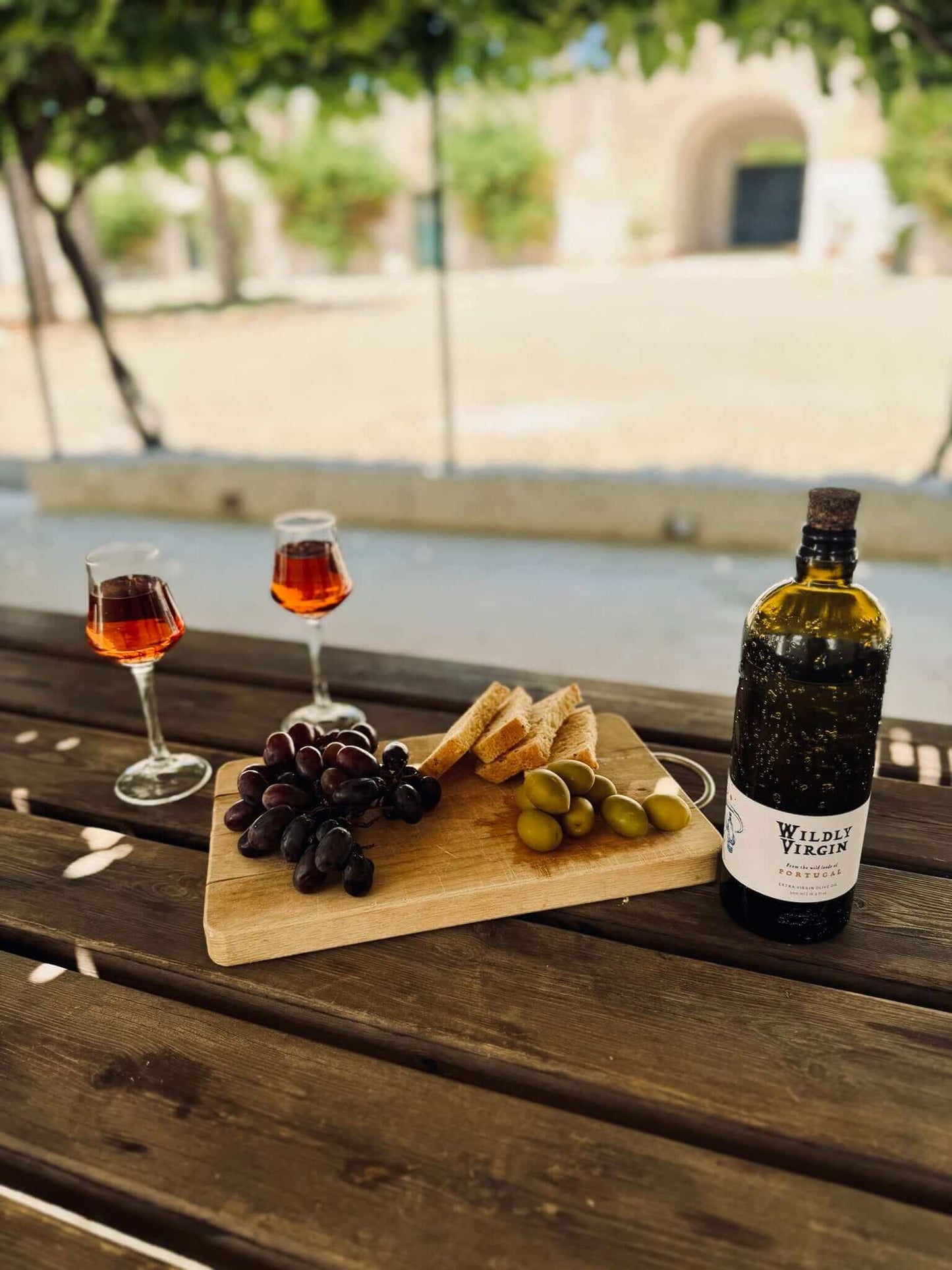 Wildly Virgin Portuguese olive oil sitting on a picnic table with grapes and rose