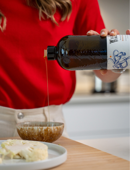 A person in a red shirt pours golden Doce olive oil into a bowl in a modern kitchen setting.