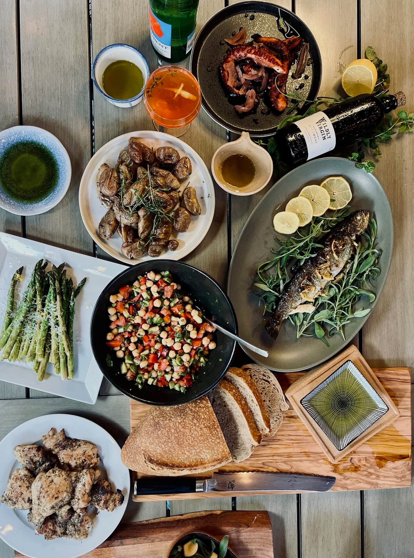 A birds-eye view of a table with bread, grilled fish, octopus, salad, chicken, and olive oil