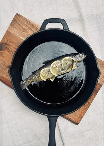 A grilled whole trout in a cast iron pan with lemon garlic and olive oil