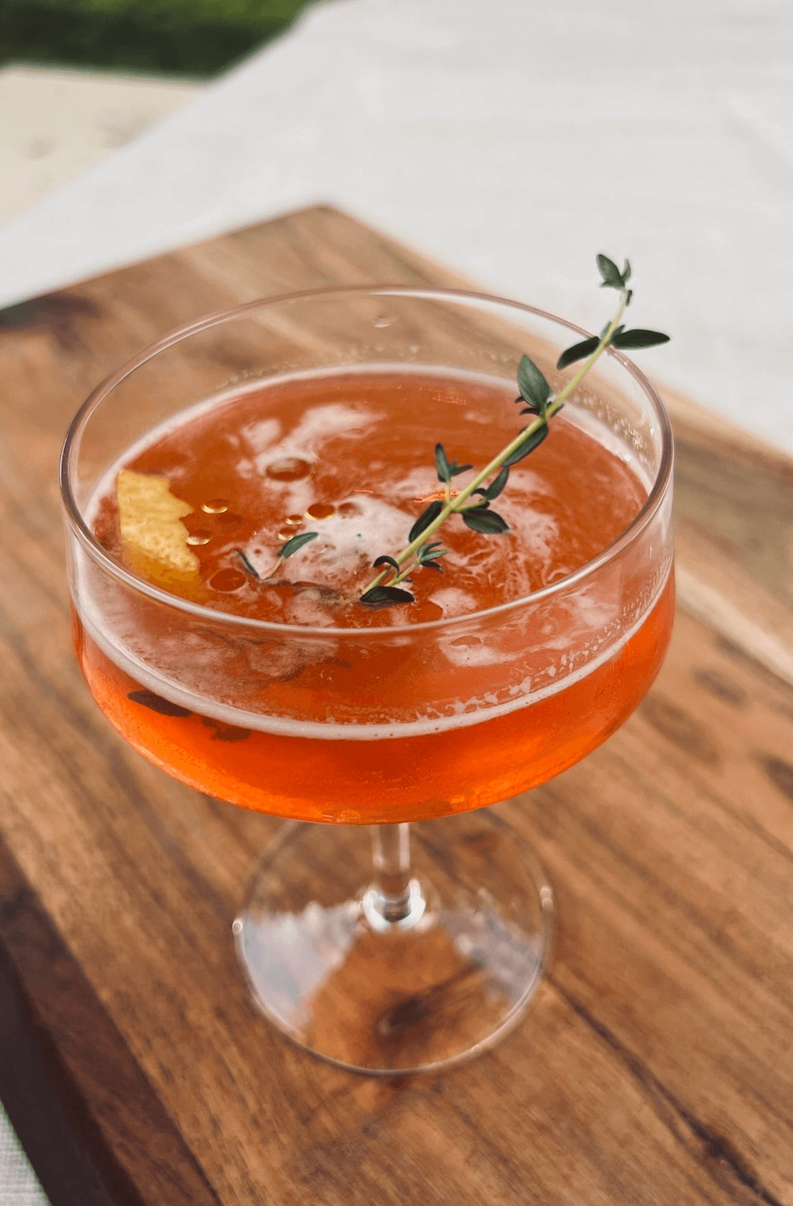 Paper airplane cocktail with olive oil drizzled over it and a sprig oh thyme