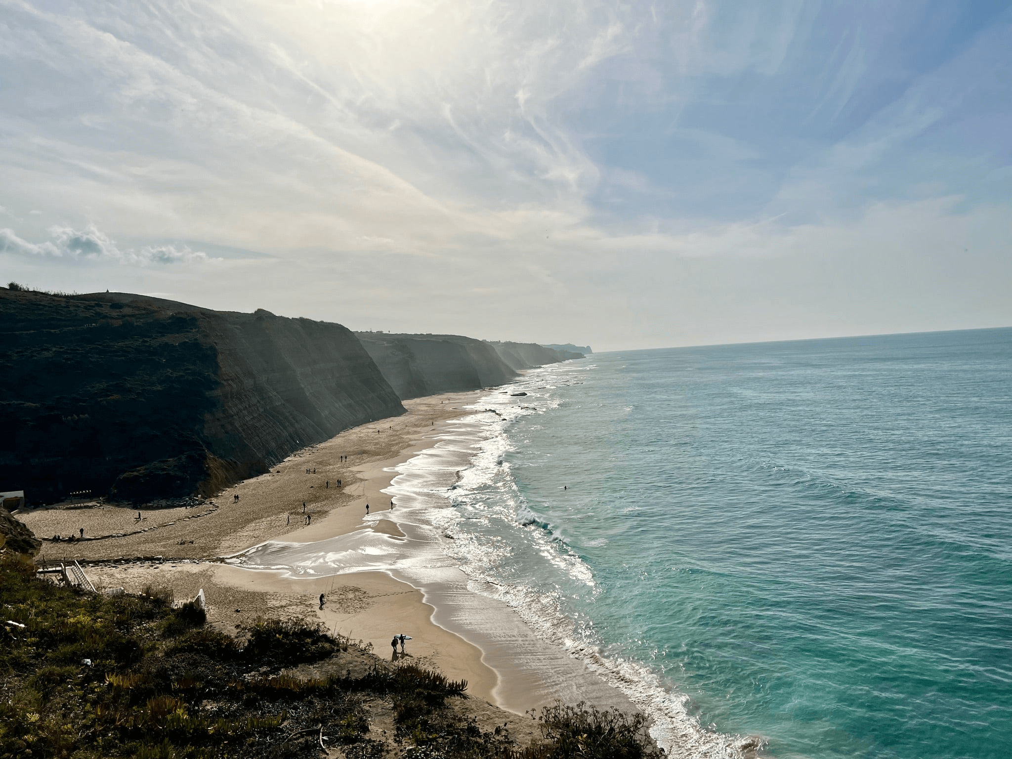 A photo of a beach in Portugal with large black cliffs and mist rising fro the ocean