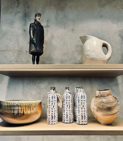 Multiple bottles of olive oil in sardine tissue wrap on a shelf with other pottery