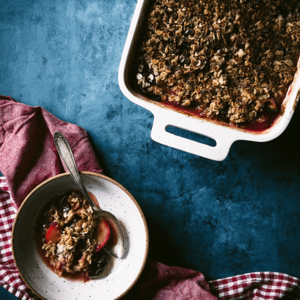 Delicious baked oatmeal with fruit served in a bowl beside the baking dish on a blue backdrop.