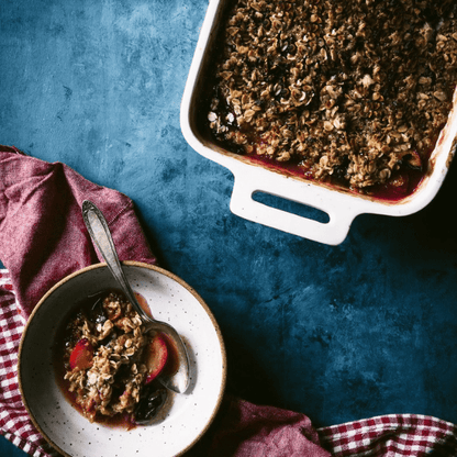 Delicious baked oatmeal with fruit served in a bowl beside the baking dish on a blue backdrop.
