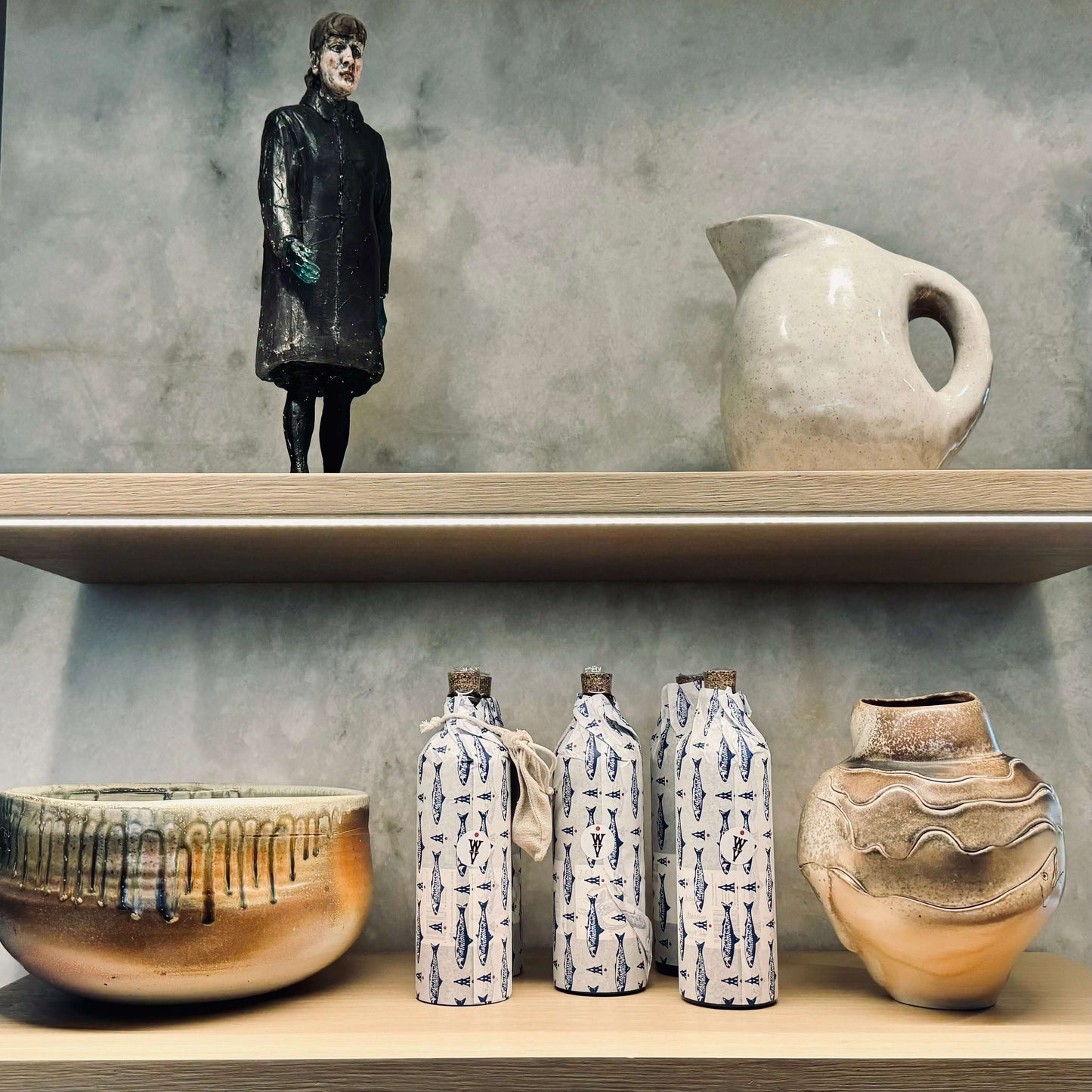 Multiple bottles of olive oil in sardine tissue wrap on a shelf with other pottery